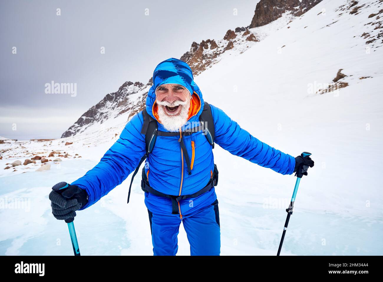 Tourist mit weißem Bart und Rucksack zu Fuß auf blauem Eis Gletscher in der wunderschönen Landschaft des Gebirgstals mit Schnee bedeckt in Almaty, Kasachstan Stockfoto