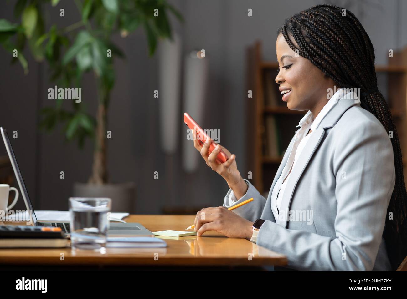 Junge lächelnde afrikanische Geschäftsfrau im Büro hält Smartphone SMS mit einem angenehmen Lächeln lesen Stockfoto