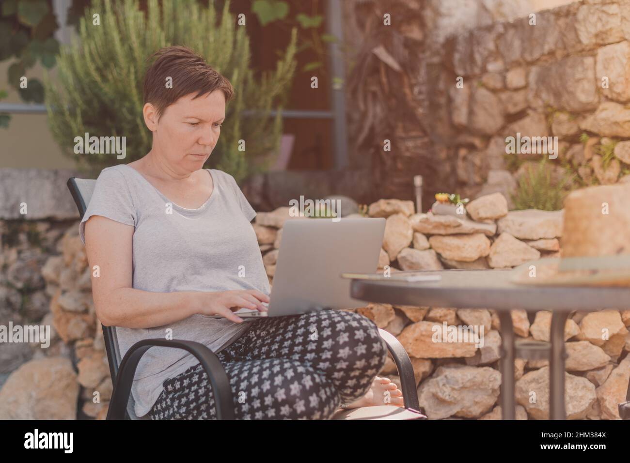 Seriöse freiberufliche Frau und digitale Nomade arbeiten auf Laptop-Computer während der Sommerferien Urlaub auf der Terrasse der Wohnung am Morgen Stockfoto