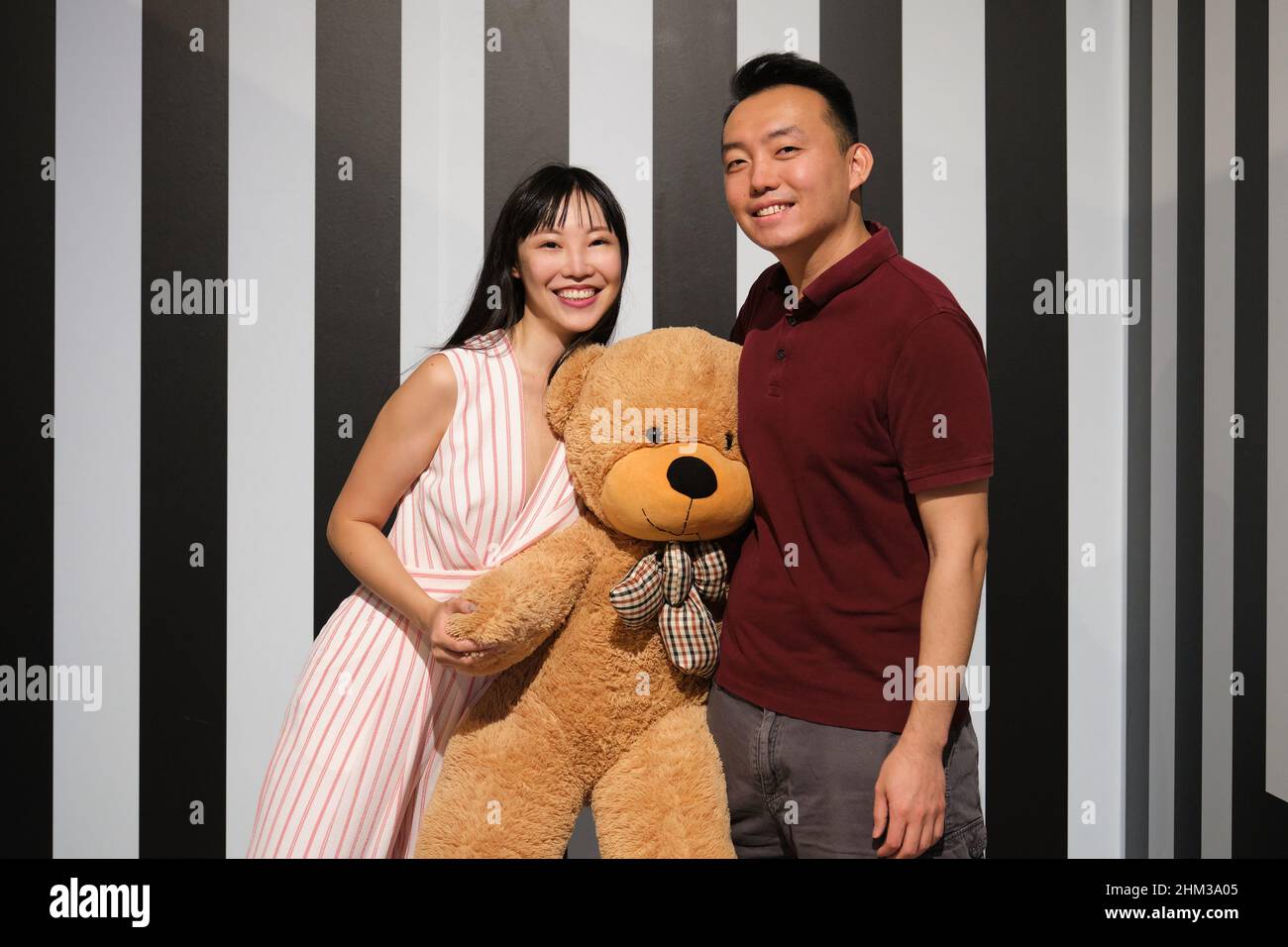 Junges asiatisches Paar mit einem großen Teddybären, der lächelt und die Kamera anschaut. Stockfoto