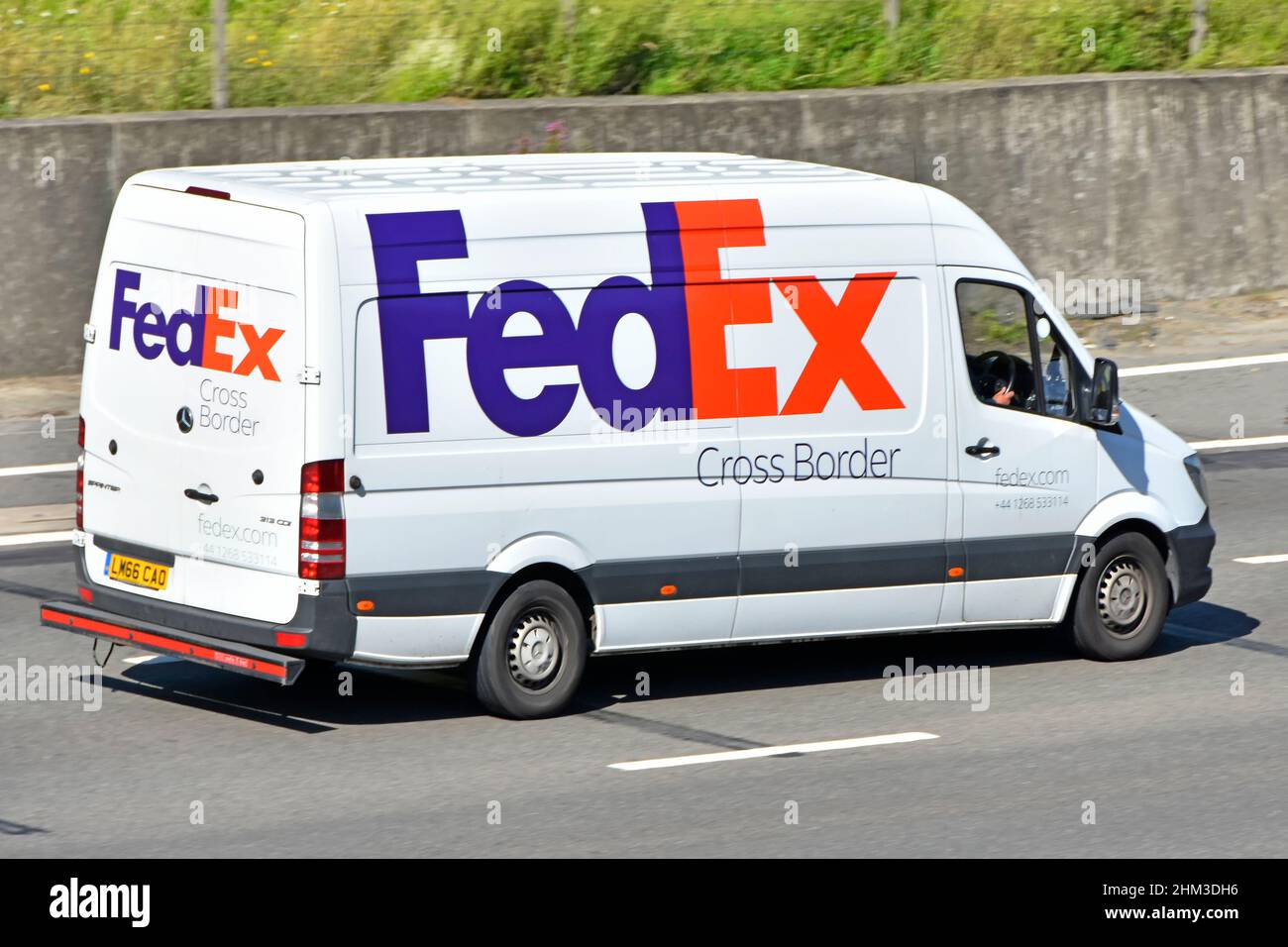 FedEx rot-blaues Firmenlogo auf der Seitenrückseite der grenzüberschreitenden Paketzustellung Lieferwagen und Fahrer, die auf der britischen Autobahn unterwegs sind Stockfoto