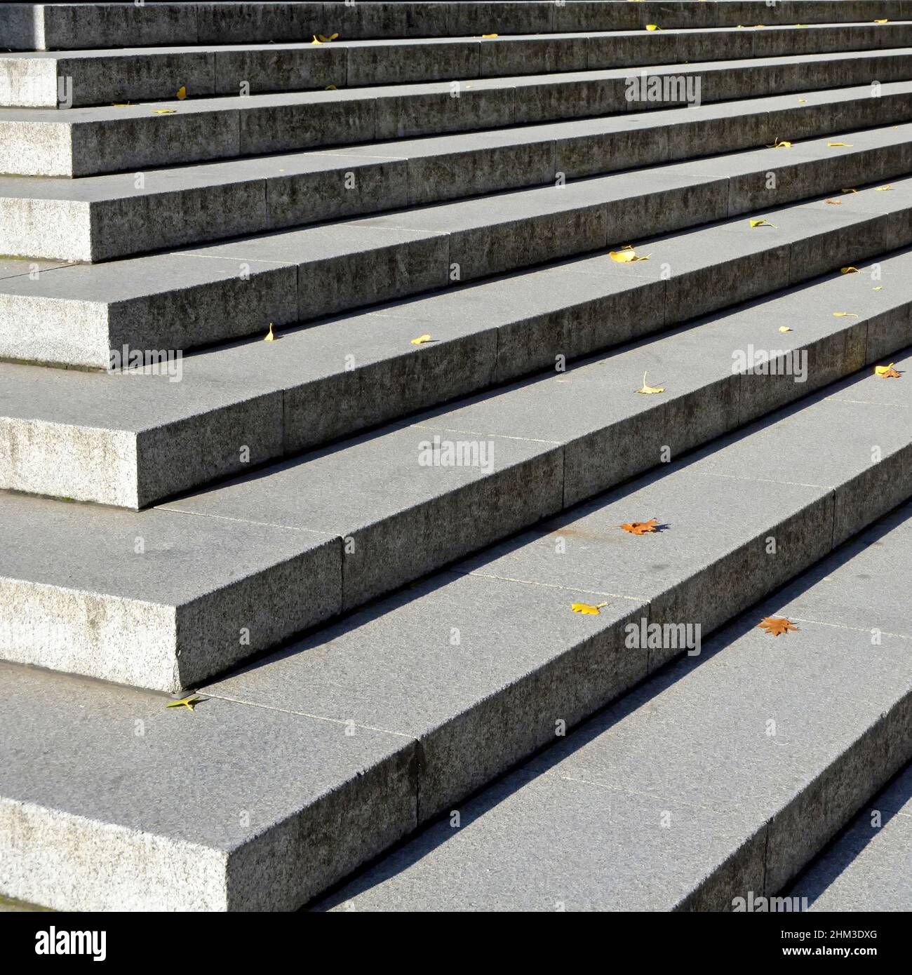 Nahaufnahme einer geraden Linie von breiten Steintreppen bei Sonnenschein Aufsteigen im Schatten auf Ecktreppen in der City of London, die mit Herbstblättern bestreut sind England Großbritannien Stockfoto