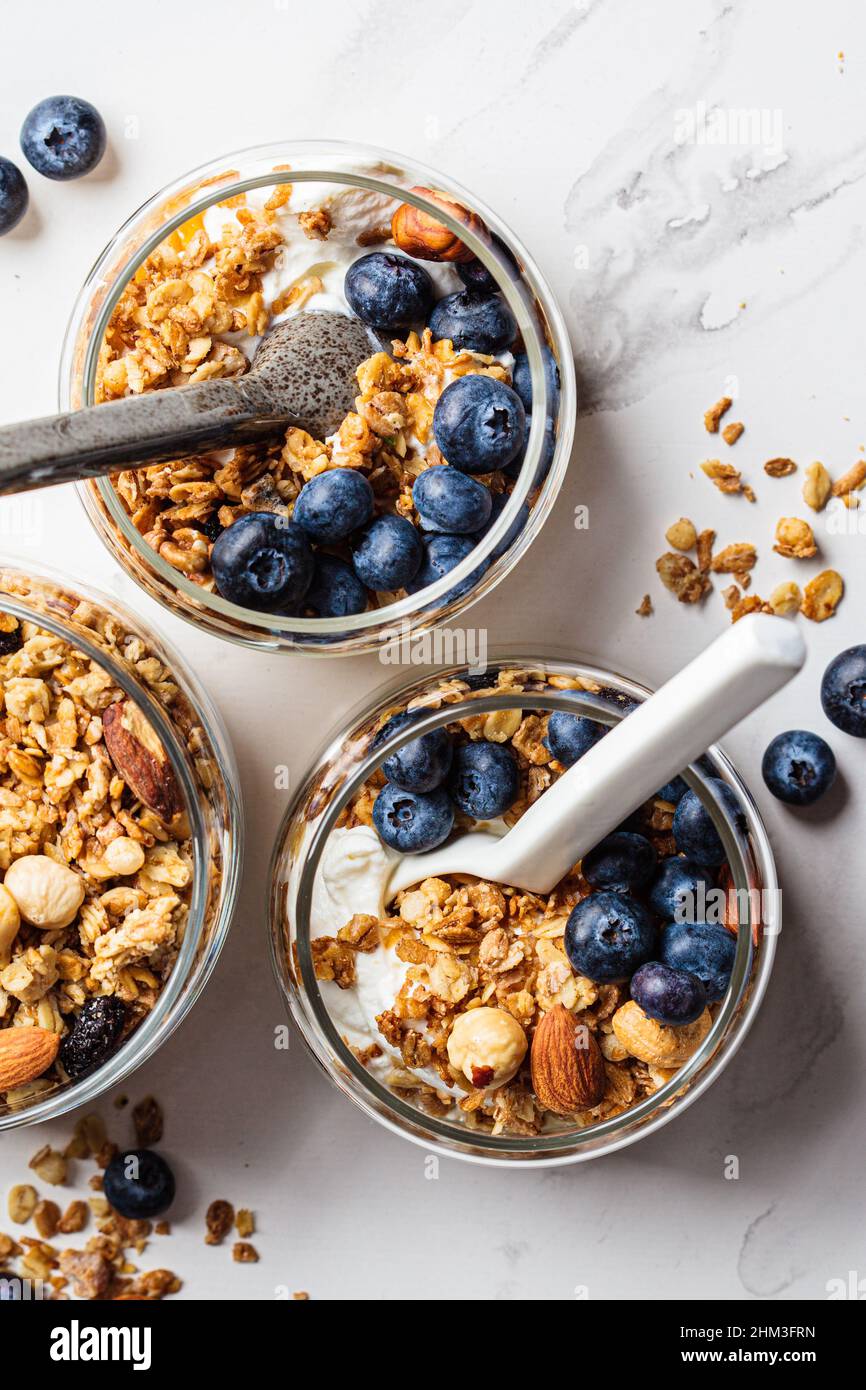 Müsli mit Nüssen, Joghurt und Beeren im Glas, Draufsicht. Frühstücksparfait mit Müsli, Joghurt und Heidelbeeren, weißer Hintergrund Stockfotografie