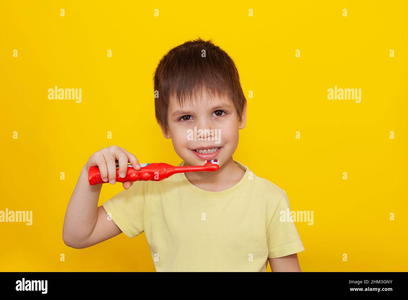 Glücklicher Kleinkind Junge Zähneputzen mit einer Zahnbürste auf gelbem Hintergrund. Gesundheitsversorgung, Mundhygiene. Ein Ort für Ihren Text. Stockfoto