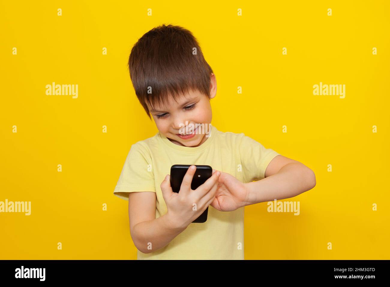 Kleines Kind spielt Spiele auf dem Smartphone auf gelbem Hintergrund. Das Konzept der modernen Bildung. Speicherplatz kopieren, Stockfoto