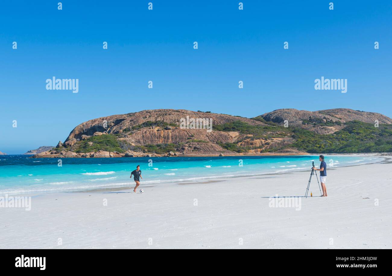 Junger Mann fotografiert eine junge Frau, die am Strand der berühmten Hellfire Bay, Cape Le Grand, in der Nähe von Esperance, Westaustralien, mit einem Fußballspiel spielt Stockfoto