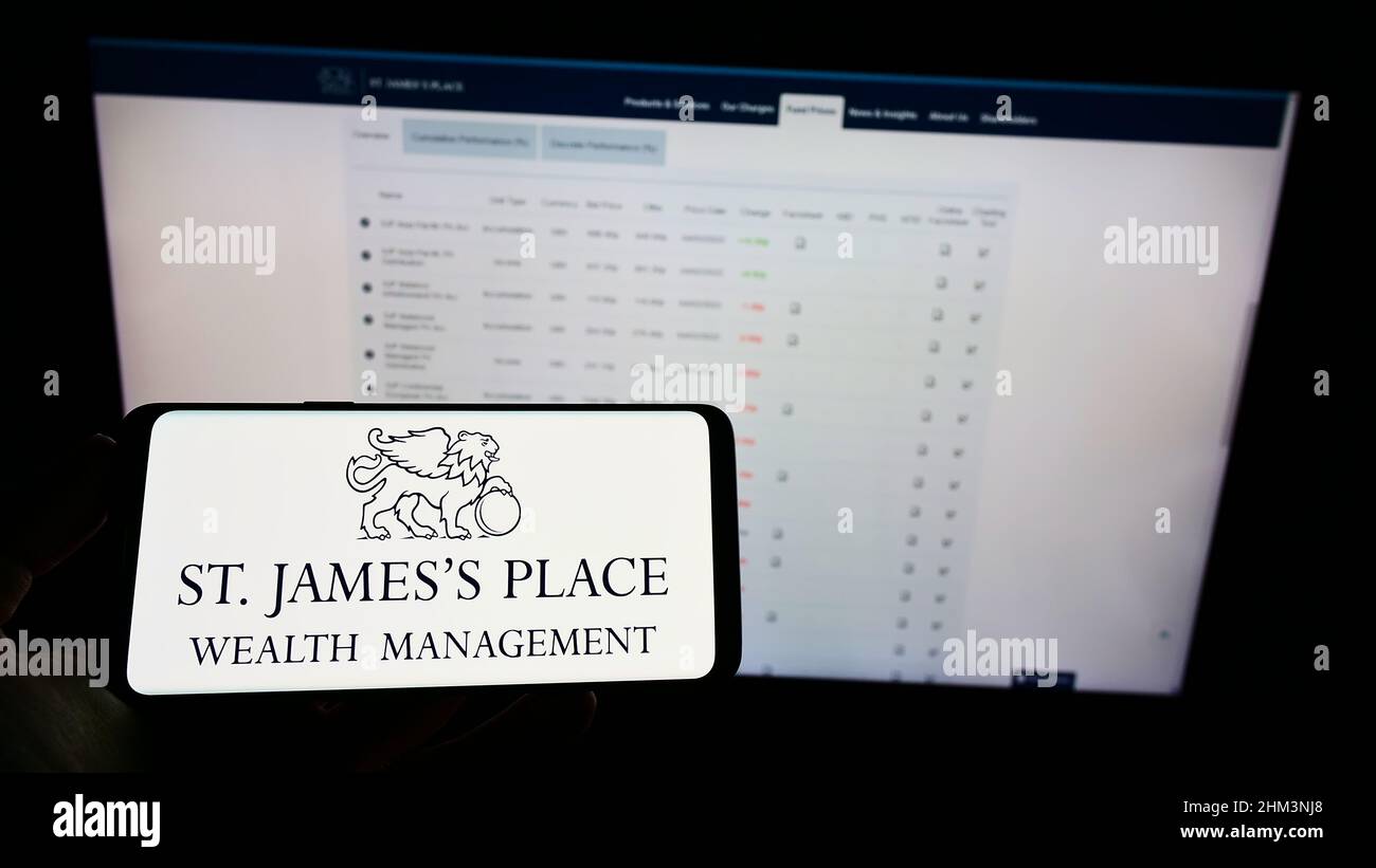 Person mit Mobiltelefon und Logo der britischen Firma St. James's Place plc auf dem Bildschirm vor der Business-Webseite. Konzentrieren Sie sich auf die Telefonanzeige. Stockfoto