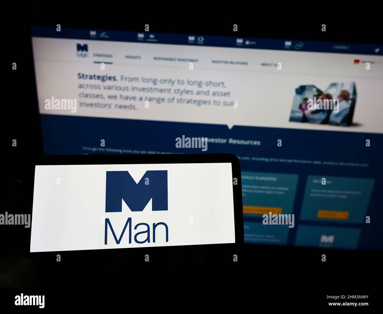 Person, die Mobiltelefon mit dem Logo des britischen Finanzunternehmens man Group plc auf dem Bildschirm vor der Business-Webseite hält. Konzentrieren Sie sich auf die Telefonanzeige. Stockfoto