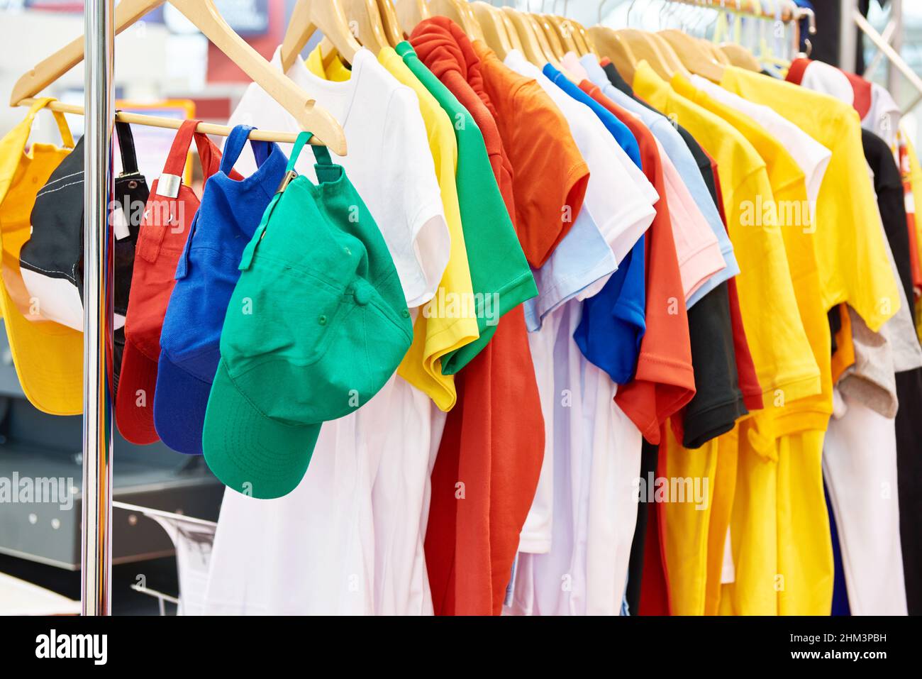 Farbige T-Shirts und Kappen auf dem Kleiderbügel im Laden Stockfoto