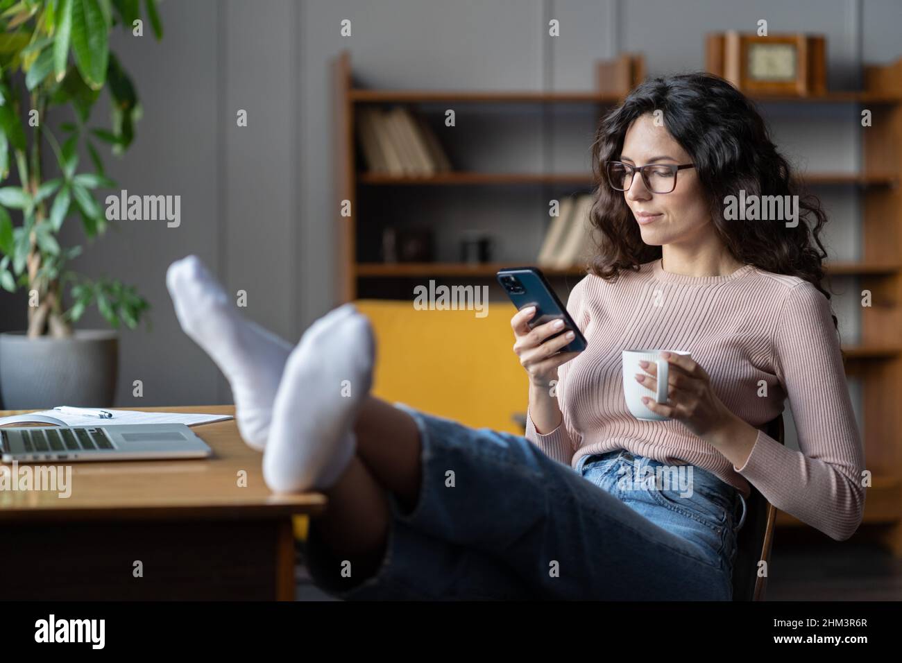 Freiberufliche Mitarbeiterin zögerlich von der Arbeit. Weibliche abgelenkt von Laptop scrollen Social Media auf dem Telefon Stockfoto