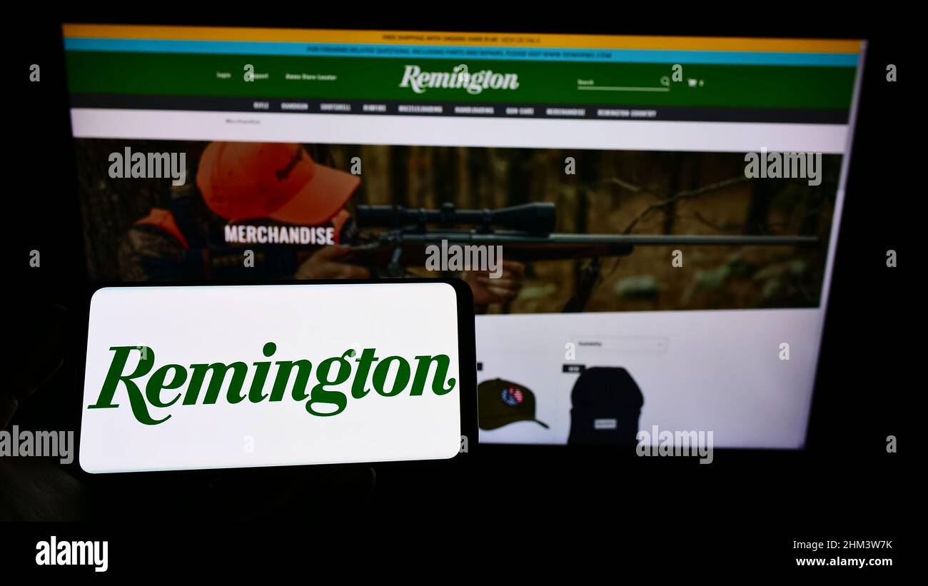 Person mit Mobiltelefon und Logo der US-amerikanischen Firma RemArms LLC (Remington Arms) auf dem Bildschirm vor der Business-Webseite. Konzentrieren Sie sich auf die Telefonanzeige. Stockfoto