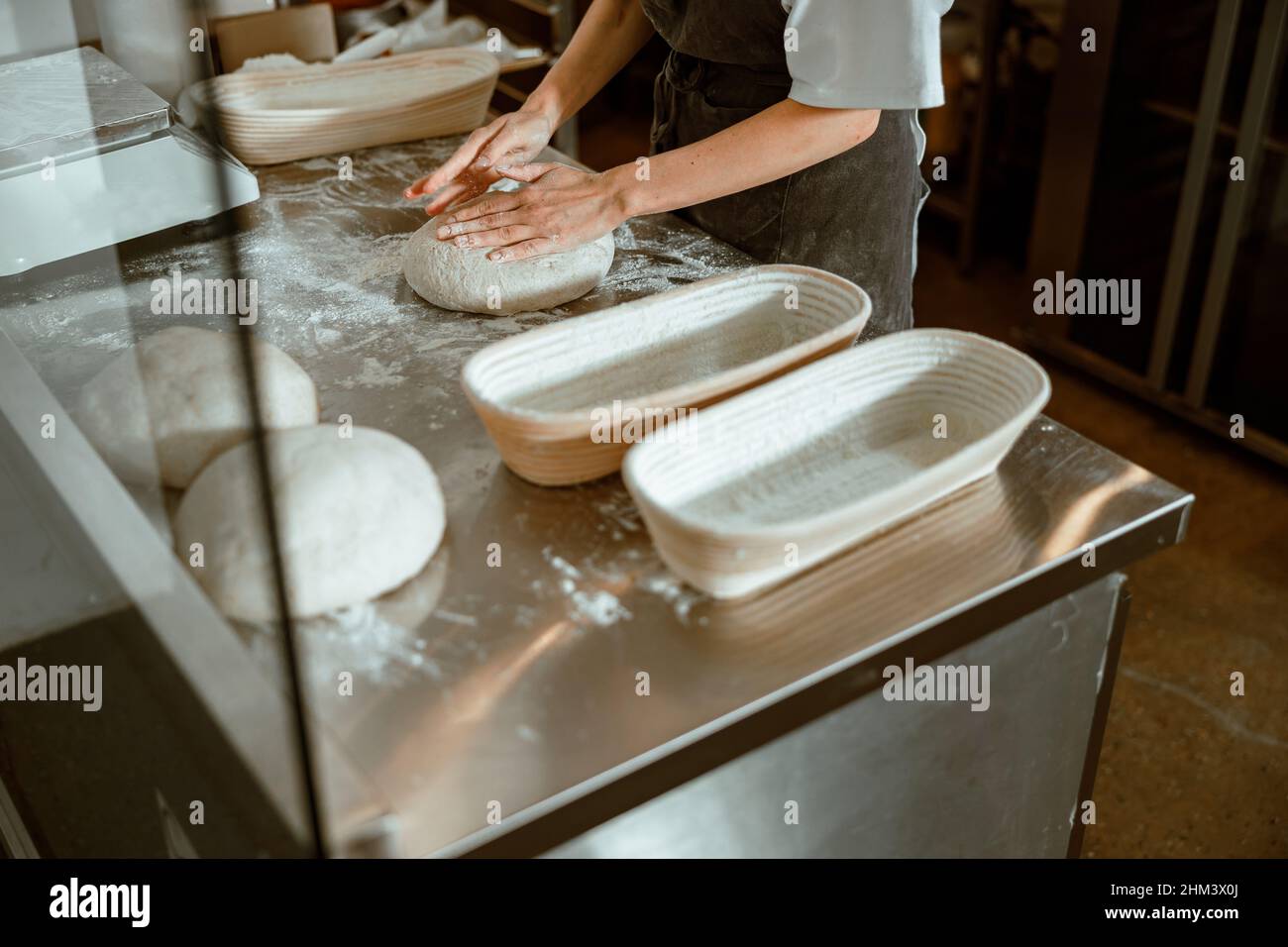 Der Mitarbeiter knetet Teig für Brot am Tisch mit Geschirr in der handwerklichen Bäckerei Stockfoto