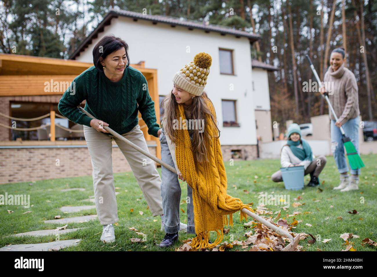 Glückliche kleine Mädchen mit Großmutter und Mutter Reinigung Garten von Blättern im Herbst Stockfoto