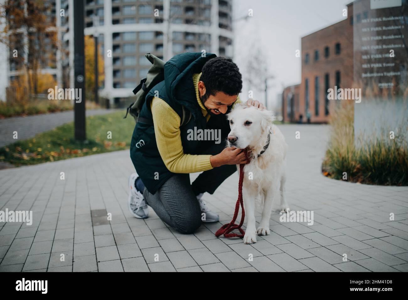 Glücklicher junger Mann, der während eines Spaziergangs im Freien in der Stadt seinen Hund hockt und streichelte. Stockfoto