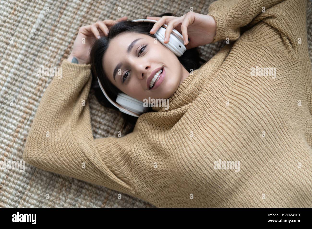 Porträt einer entspannten Frau, die zu Hause mit Kopfhörern auf einem Teppich Musik hört Stockfoto