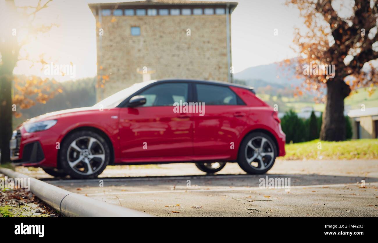 Blur Red SUV auf dem Parkplatz im Freien der Stadt geparkt. Seitenansicht des Elektroautos auf dem Parkplatz. Elektrofahrzeug-Konzept. Roadtrip Reisen in Europa. Stockfoto