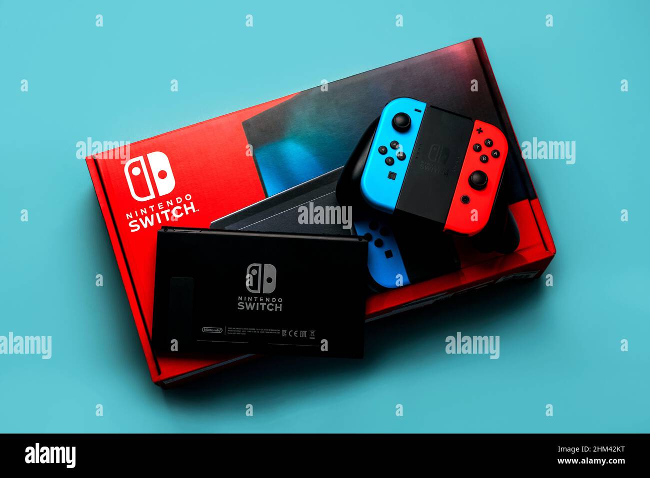 Nintendo Switch Videospielkonsolenbox mit Nintendo Switch Logo, Rückseite von Nintendo Switch und zwei Joy-Cons auf blauem Hintergrund Stockfoto