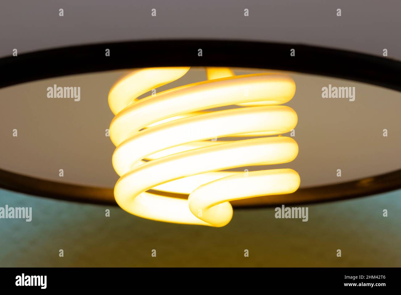 Nahaufnahme einer glühenden, energieeffizienten Spirallampe, die an der Wandlampe klebt Stockfoto