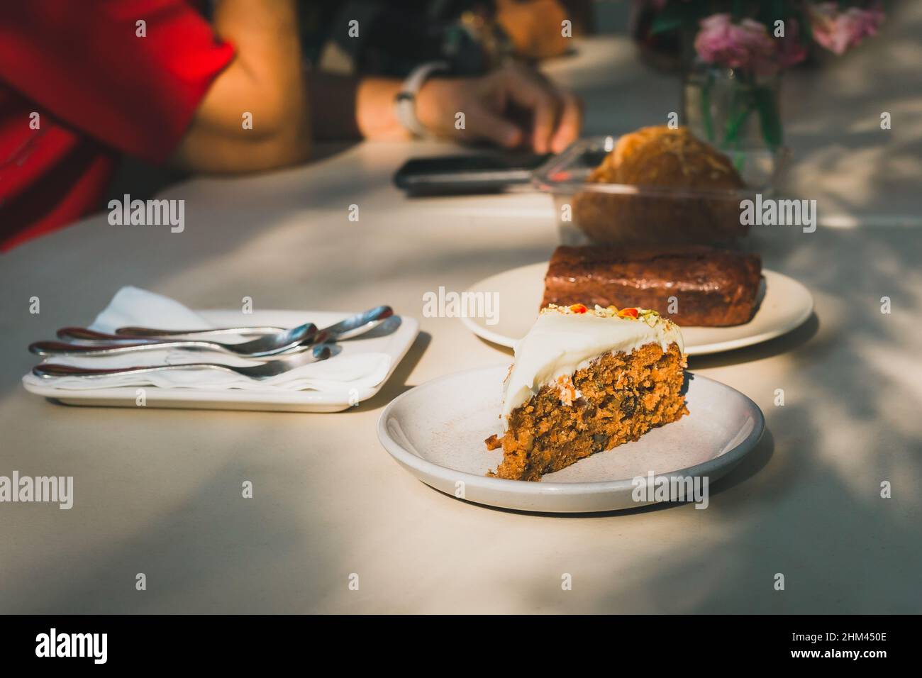 Ein Stück Karottenkuchen auf dem Tisch mit einer Frau im Hintergrund in einem Café. Stockfoto