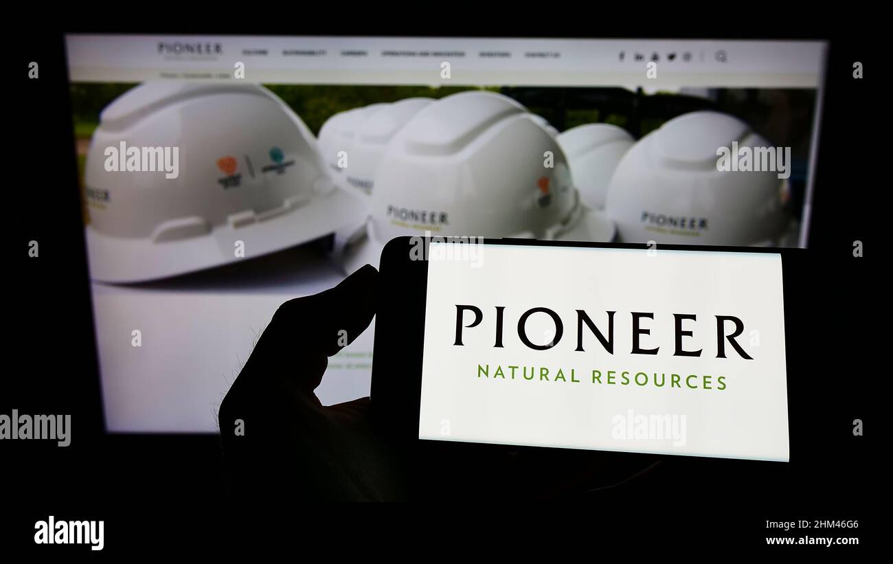 Person, die Mobiltelefon mit Logo des amerikanischen Unternehmens Pioneer Natural Resources Company auf dem Bildschirm vor der Webseite hält. Konzentrieren Sie sich auf die Telefonanzeige. Stockfoto