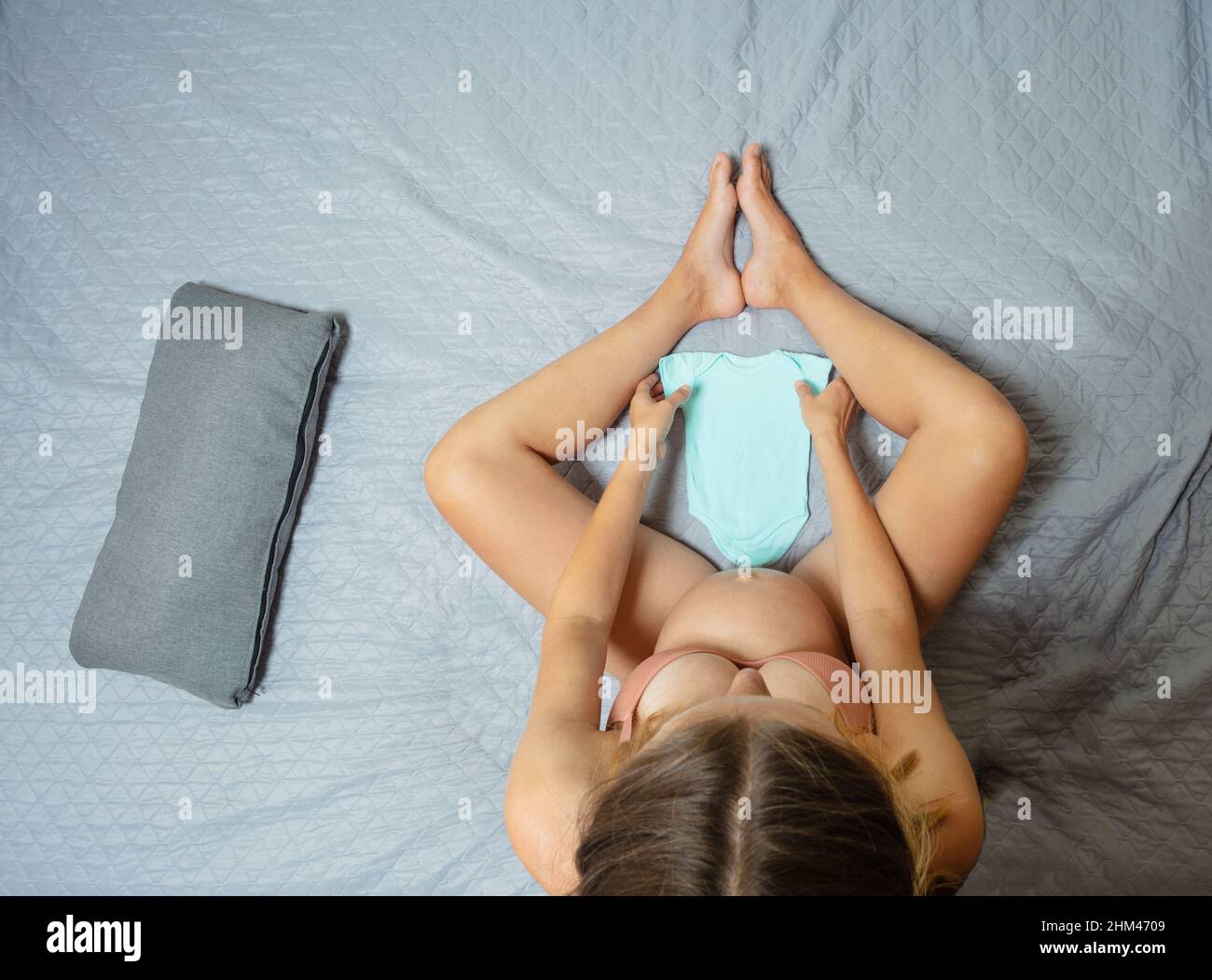 Frau sitzt auf dem Bett und hält Babykleidung Stockfoto