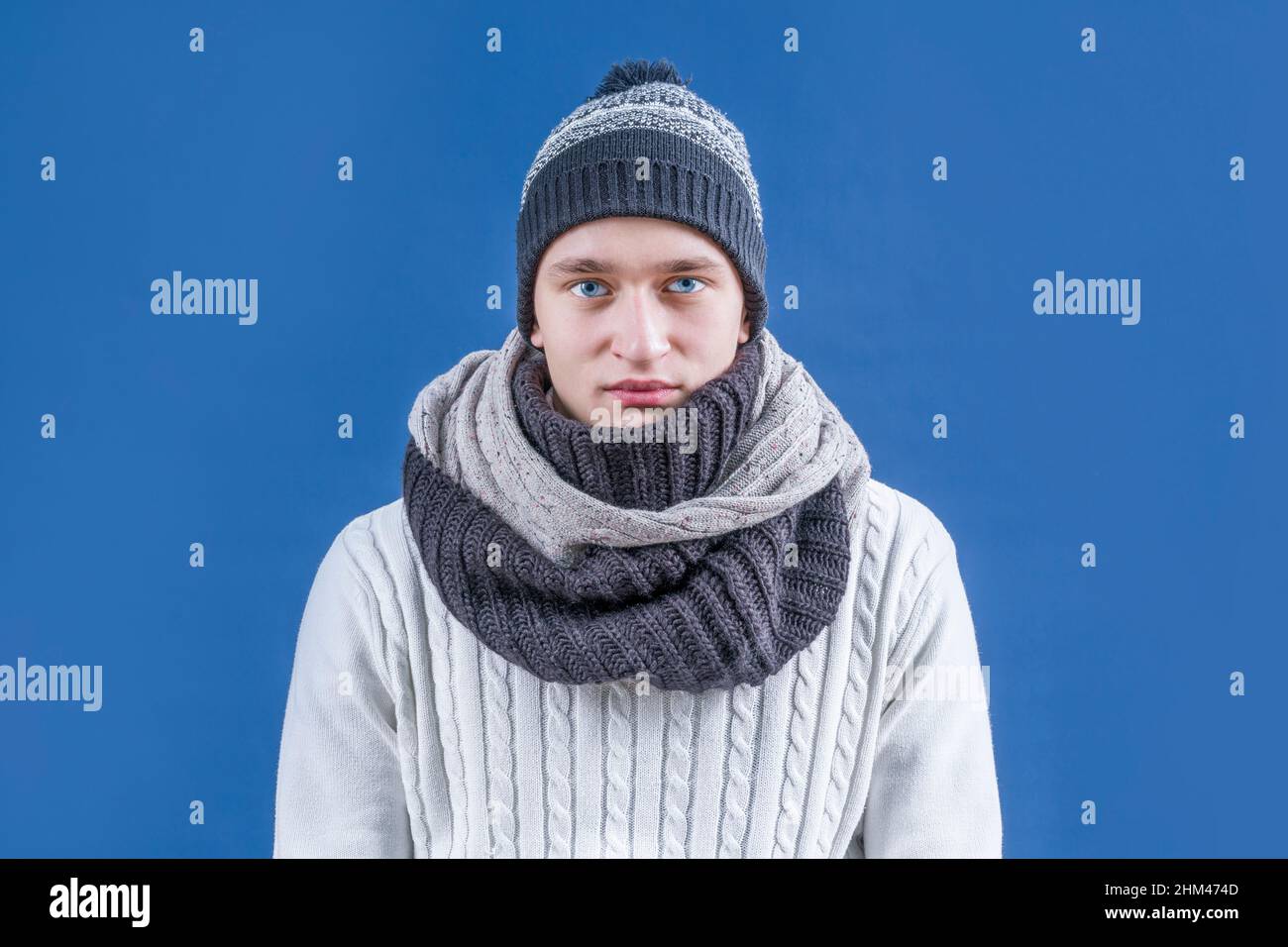 Winter. Winterkleidung. Ein Mann in einem weißen Pullover, Schal und Winterhut sitzt ruhig und blickt auf die Kamera. Stockfoto