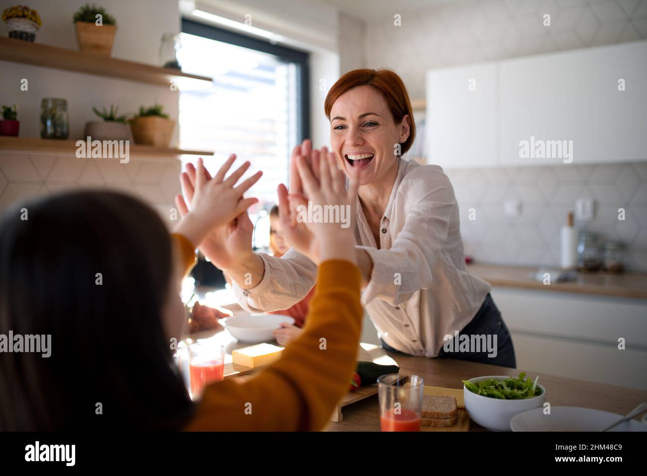 Glückliche Mutter von drei kleinen Kindern, die zu Hause in der Küche Lunchboxen zubereiten. Stockfoto