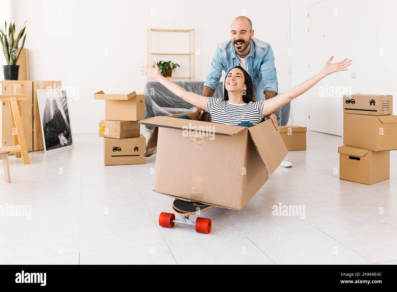 Glückliches Paar, das Spaß beim Auspacken am Umzugstag in einer neuen Wohnung hat Stockfoto
