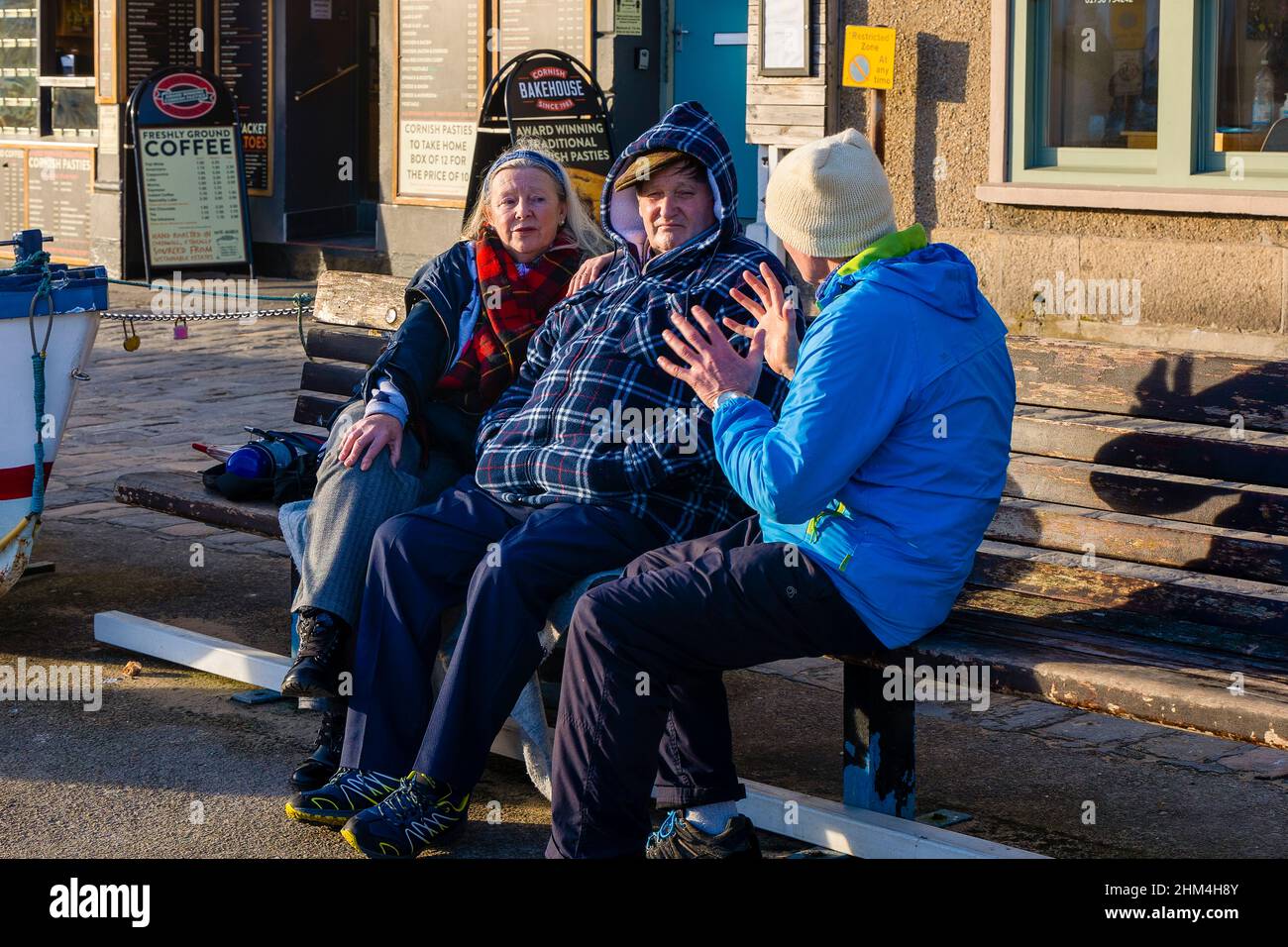 Die Diskussion. Drei Personen saßen auf einer Bank an der Hafenfront und genossen die letzte der untergehenden Wintersonne, während sie die Welt in Ordnung gebracht haben. Stockfoto