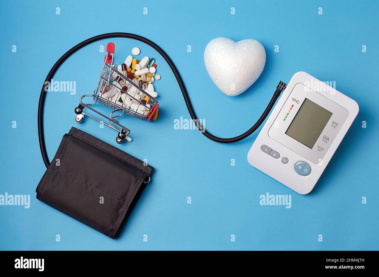 Vor einem hellblauen Hintergrund, einem Blutdruckmessgerät, einem mit Pillen gefüllten Supermarkt-Trolley, einem weißen Herz.Konzept:Medikamente für Menschen suff Stockfoto