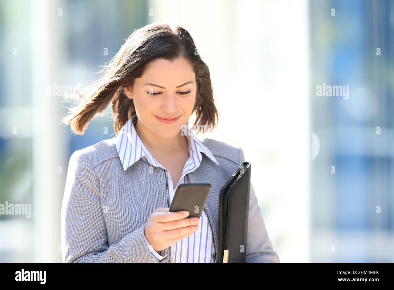 Eine zufriedene Geschäftsfrau, die ihr Smartphone überprüft und auf der Straße läuft Stockfoto
