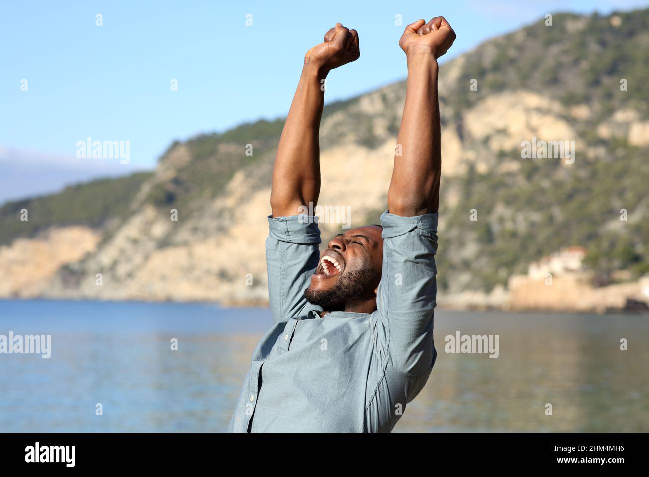Ein Mann mit schwarzer Haut, die die Arme hebt, feiert seinen Urlaub am Strand Stockfoto