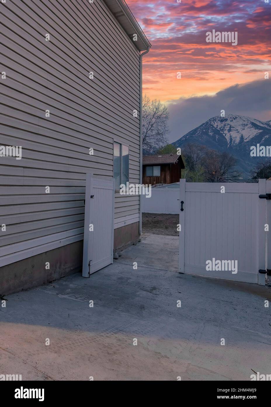 Vertikaler dramatischer Sonnenuntergang mit Wolken Seitenansicht eines zweistöckigen Hauses mit Vinylholz-Abstellgleis und einem Vie Stockfoto