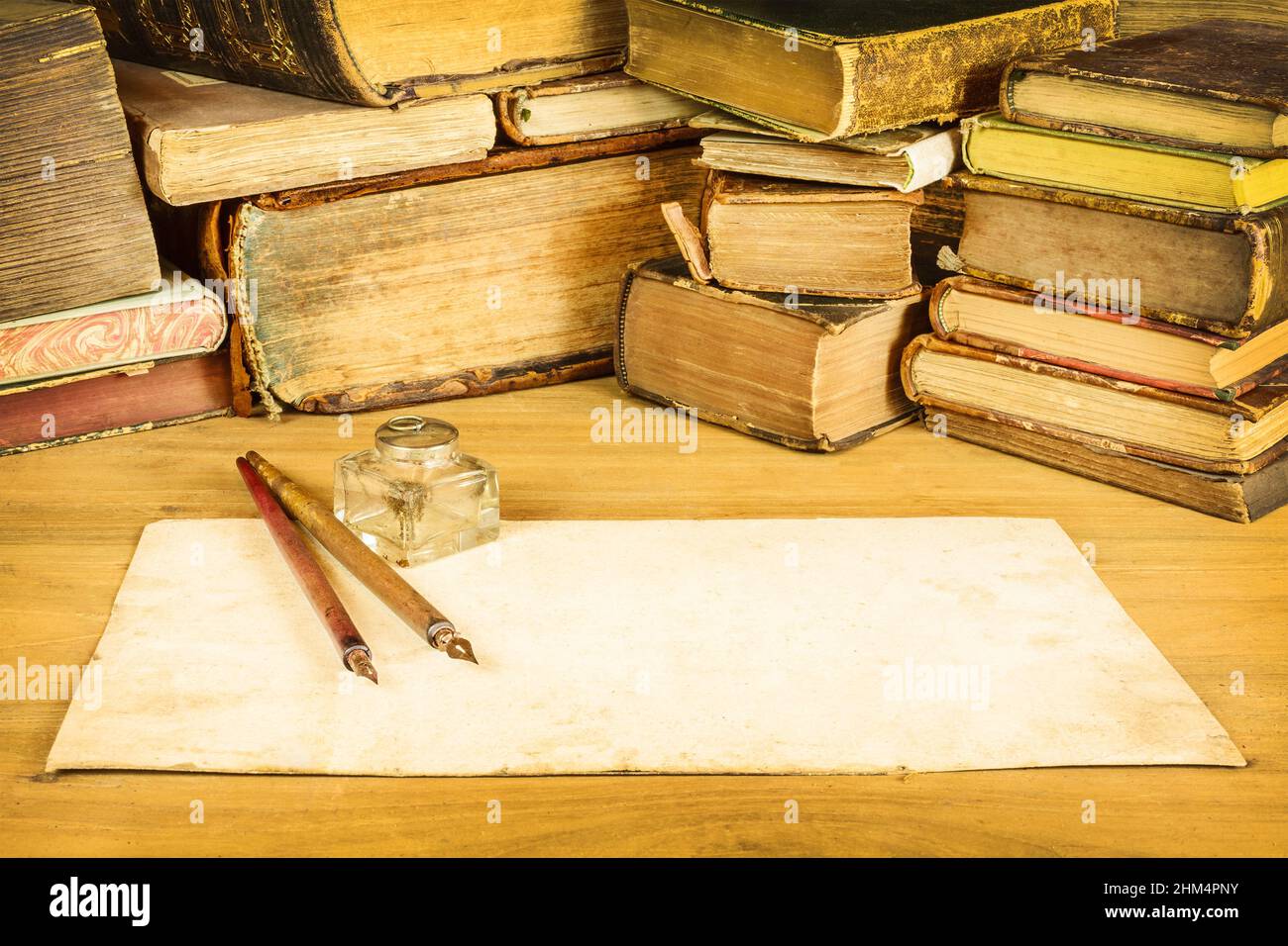 Sepiafarbtes Bild von Vintage-Füllfederhaltern mit leerem Papier vor alten Büchern auf einem Tisch Stockfoto