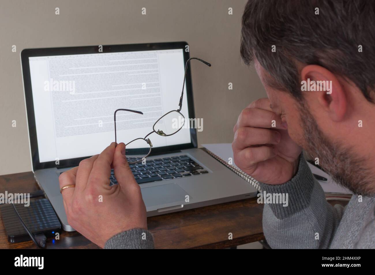 Der Mann arbeitet an einem Laptop und zieht seine Brille aus, weil seine Augen ihn stören. Brille im Vordergrund, Laptop im Hintergrund Stockfoto