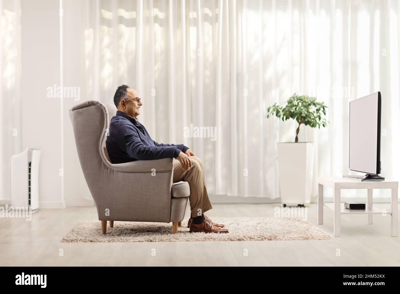 Profilaufnahme eines reifen Mannes, der in einem Sessel sitzt und zu Hause Fernsehen sieht Stockfoto