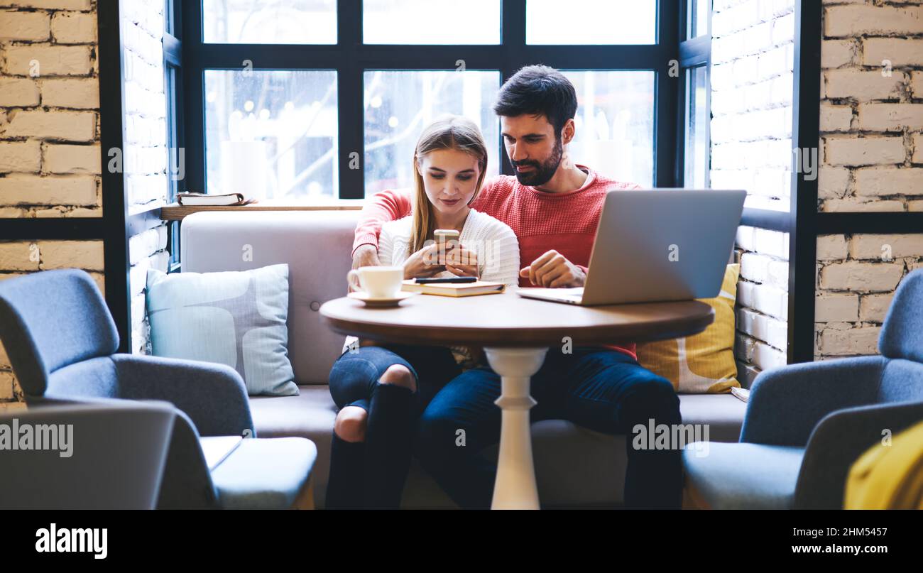 Junges Paar, das Zeit im Restaurant verbringt, während es sich Fotos auf dem Smartphone ansieht Stockfoto