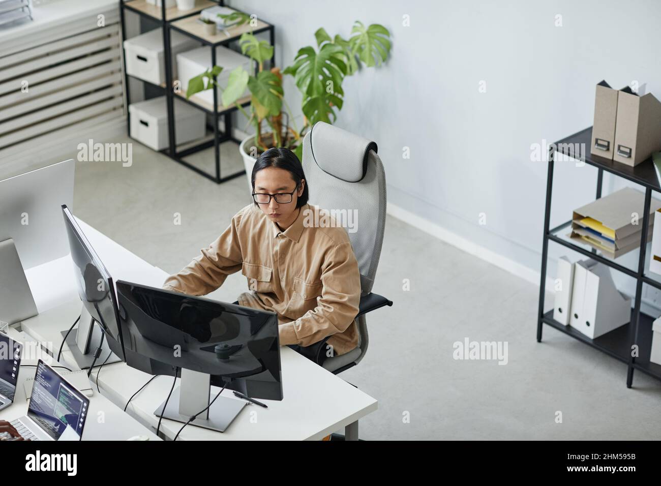 Junger seriöser männlicher Diversity-Programmierer, der aufmerksam auf den Computerbildschirm schaut, während er über die Entwicklung eines neuen Programms arbeitet Stockfoto