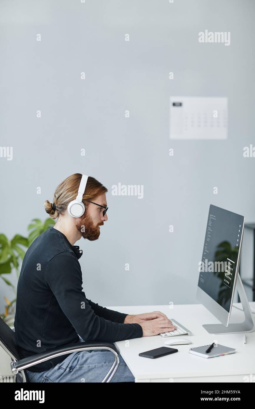 Moderner junger Programmierer für Diversität in legerer Kleidung und Kopfhörern, der vor dem Computermonitor arbeitet Stockfoto