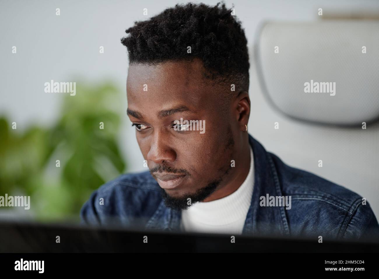 Junge ernsthafte afroamerikanische Büroangestellte, die während der Online-Kommunikation auf den Computerbildschirm schauen oder mit Daten arbeiten Stockfoto