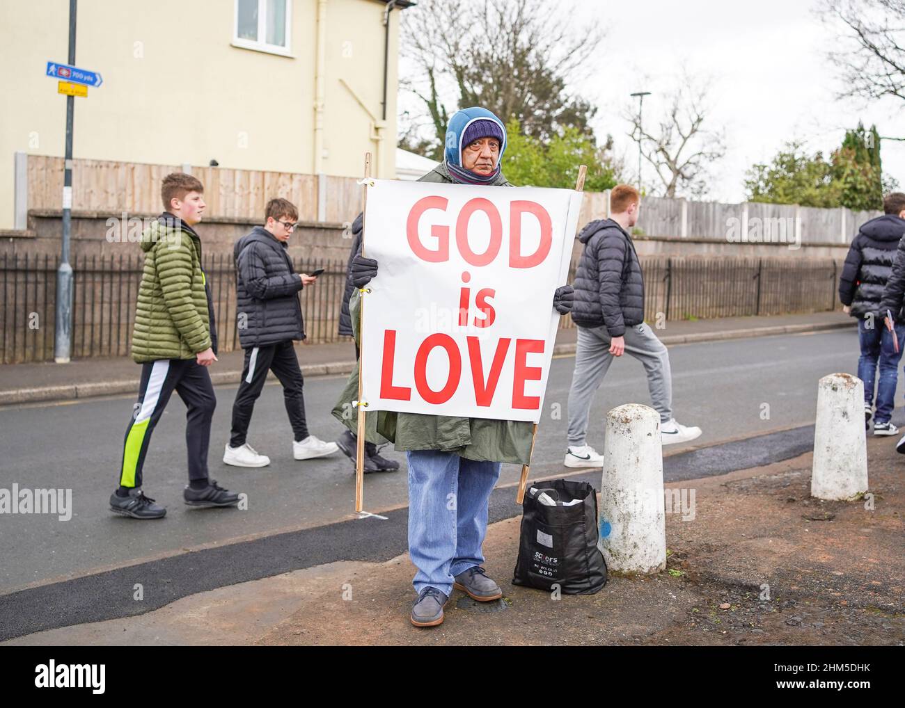 Mann, der vor dem Fußballplatz das Schild „God is Love“ zeigt, als die Fans für das Spiel „Kidderminster vs. West Ham“ in Großbritannien eintreffen. Stockfoto