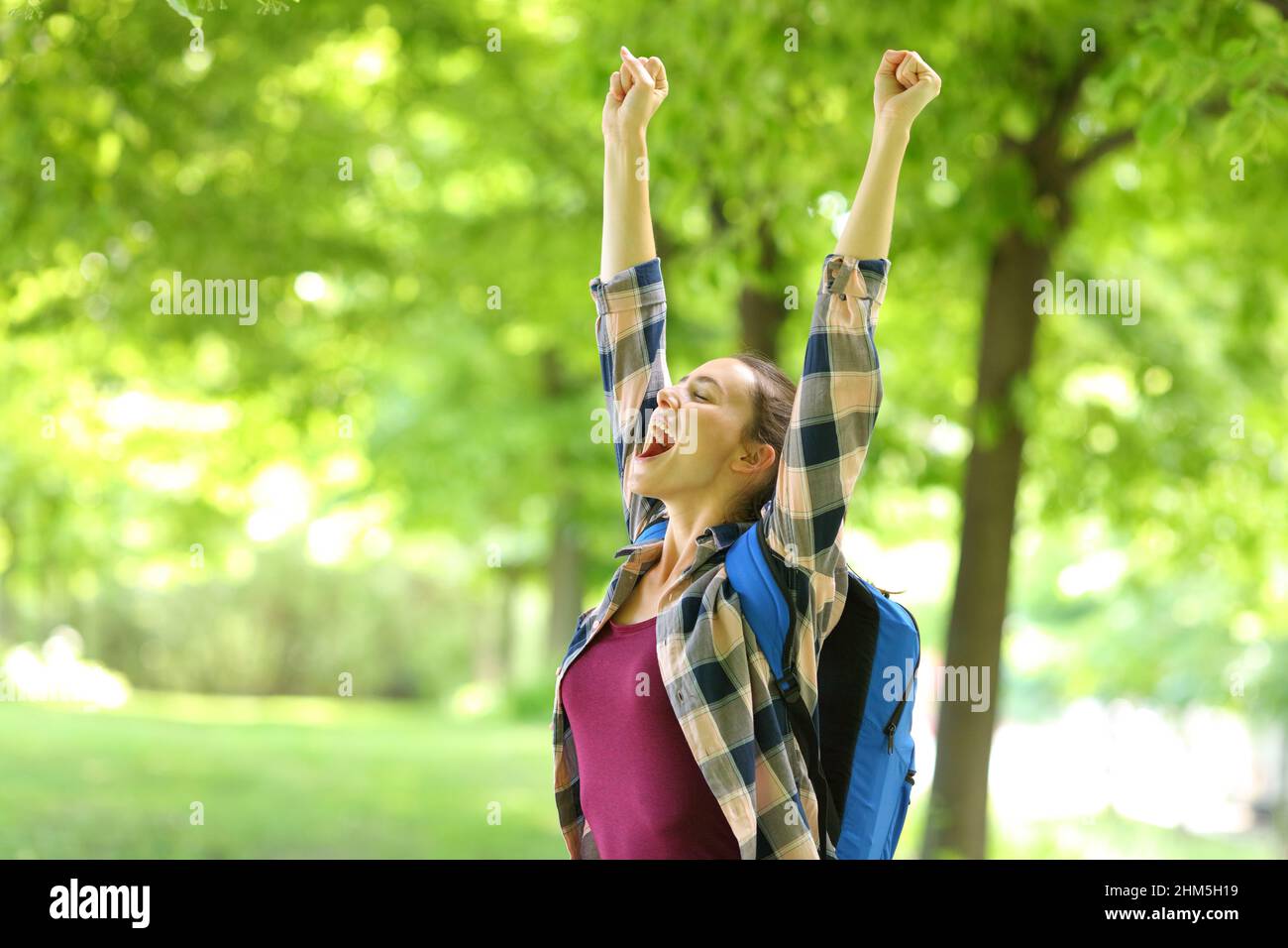 Ein begeisterter Student, der die Waffen hebt und den Erfolg in einem Park feiert Stockfoto