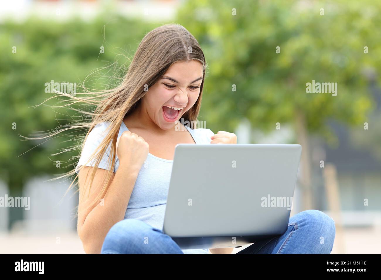 Aufgeregt teen Überprüfung gute Nachrichten auf Laptop auf der Straße Stockfoto