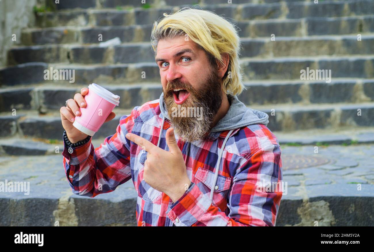 Bärtiger Mann mit Kaffee zum Mitnehmen im Freien. Guten Morgen. Fröhlicher Typ, der auf der Treppe mit einem Pappbecher sitzt. Stockfoto