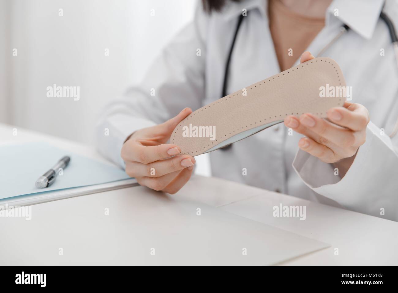 Arzt, der eine Einlegesohle hält, während er an einem Tisch sitzt. Orthopäde testet das medizinische Gerät. Orthopädische Einlagen. Fußpflege. Korrektur Der Flachen Füße Stockfoto