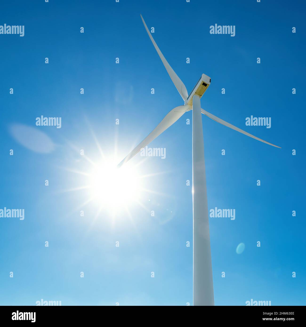 Die mit Sonne beleuchteten Rotorblätter der Windkraftanlage strahlen gegen den blauen Himmel, Lichtreflexe Stockfoto