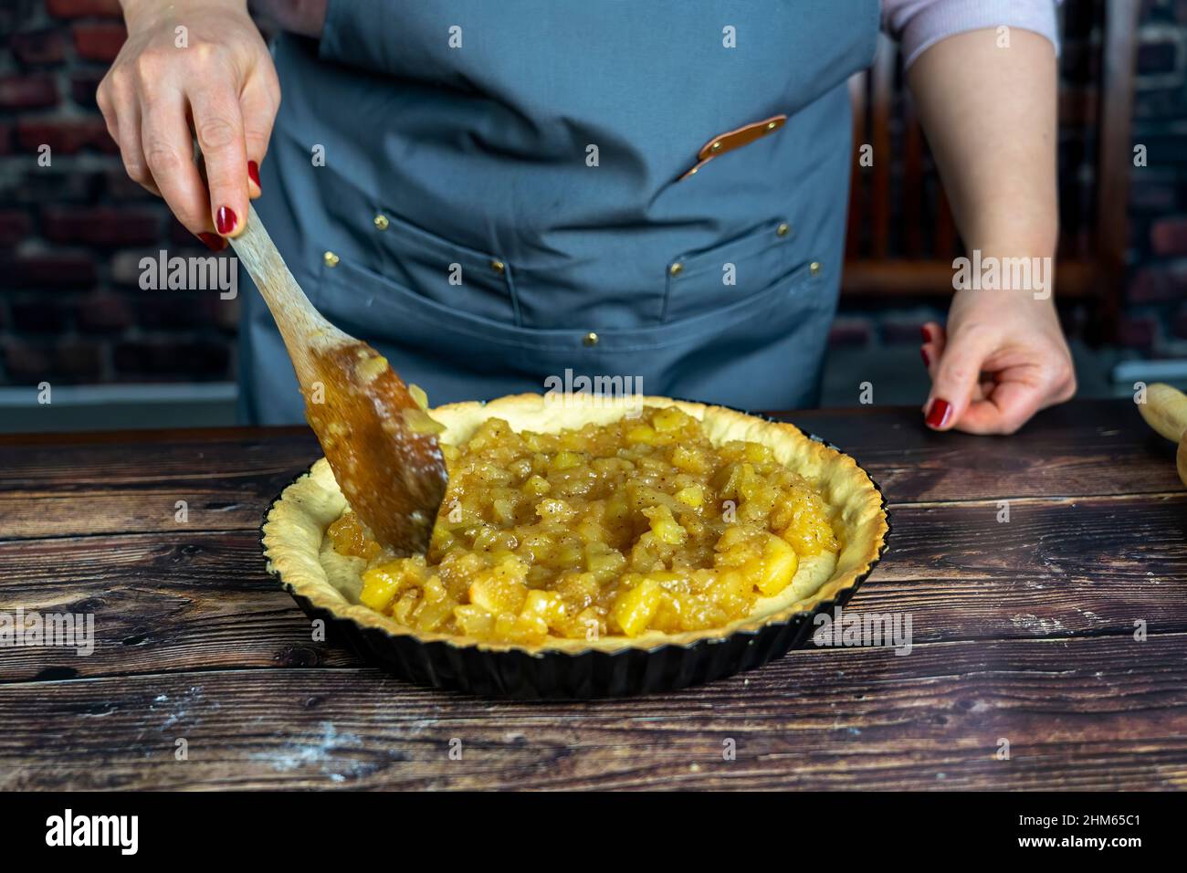 Frauen bereiten köstliche Apfeltorte oder Kuchen groß auf Holztisch Hintergrund.Spredding die gekochten kandierten Apfel über den Teig Stockfoto