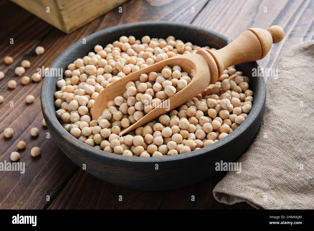 Rohe Kichererbsen in einer Schüssel. Kichererbsen in Schüssel geben und auf Holztisch auflöffeln. Stockfoto