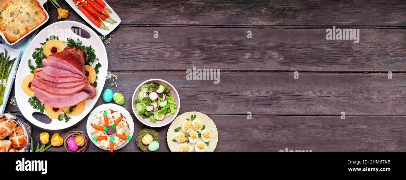 Traditionelles Abendessen mit Osterschinken. Obere Ansicht Eckrand auf einem dunklen Holz Banner Hintergrund mit Kopierraum. Schinken, Jakobsmuffel, Gemüse, Eier, h Stockfoto