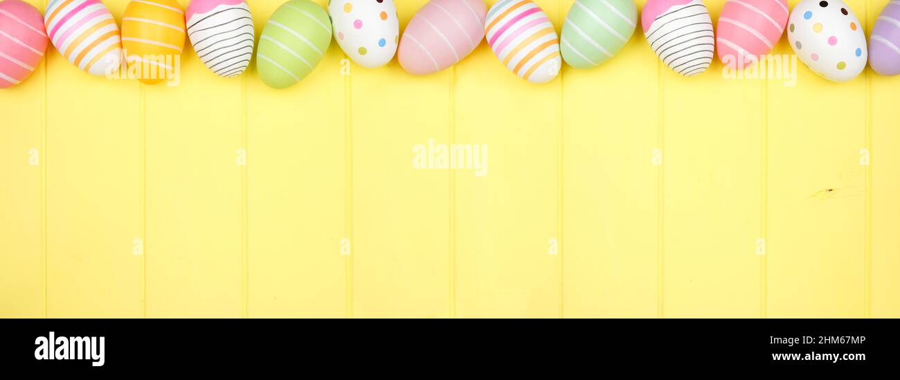 Bunte Osterei oberen Rand über einem weichen gelben Holz Banner Hintergrund. Overhead-Ansicht mit Kopierbereich. Stockfoto